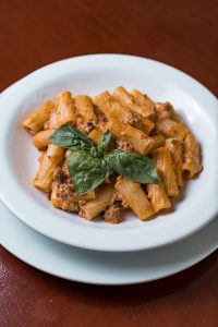 Pasta with Tomato Sauce, Meat and Fresh Basil on Top, Served on a White Plate 