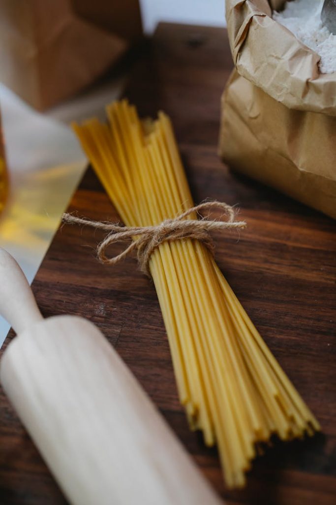 Spaghetti and rolling pin near flour on wooden surface